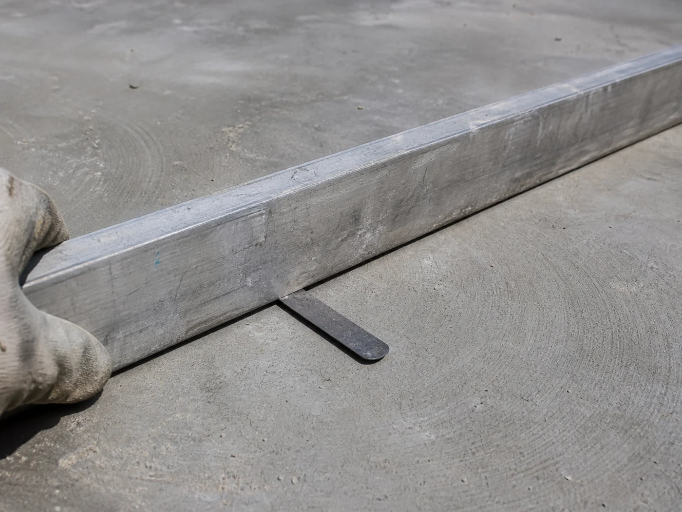Straightedge and depth gauge checking a slab for low spots before coating